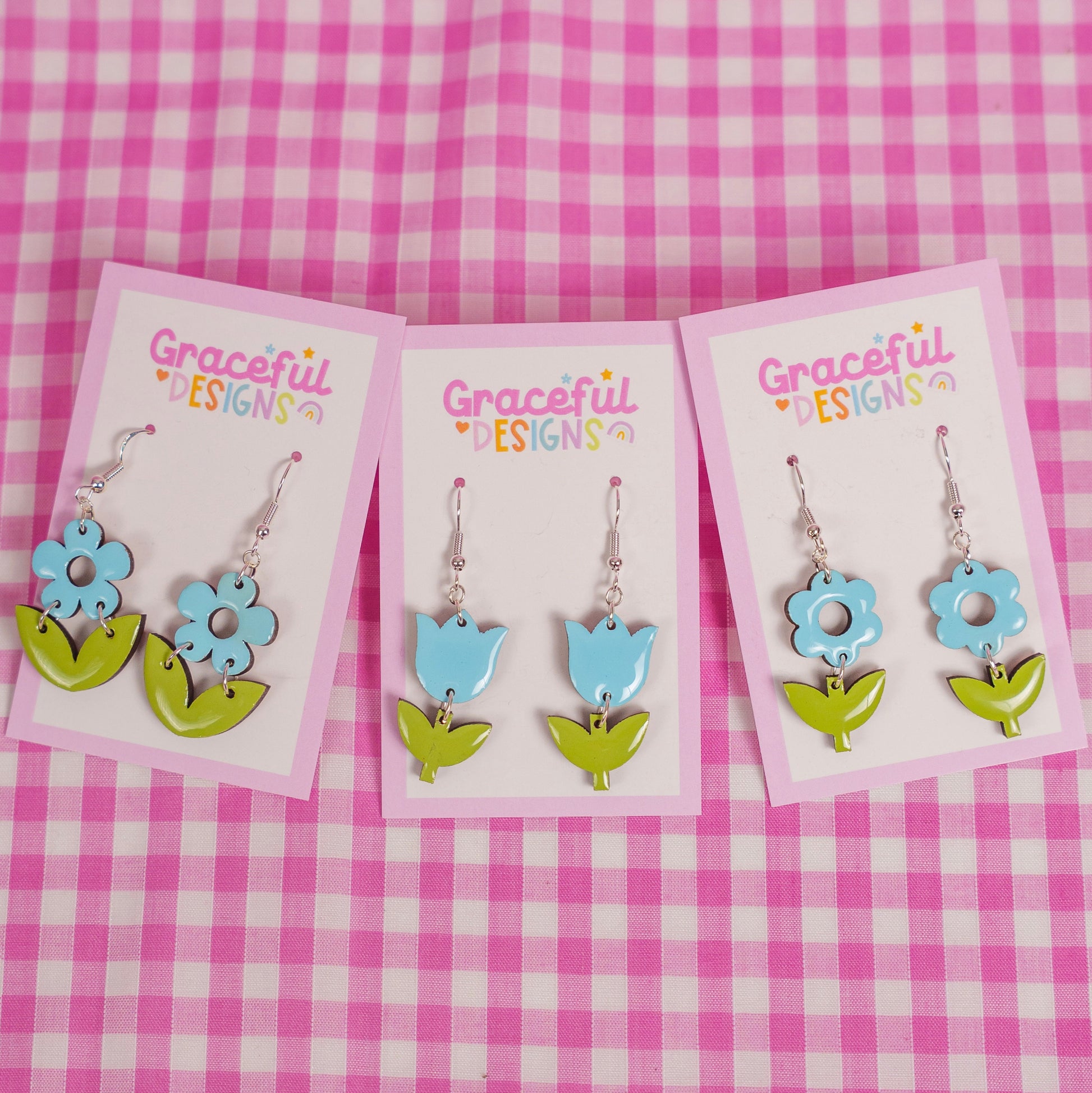 Floral earrings on cards with 'Graceful Designs' branding against a pink checkered background
