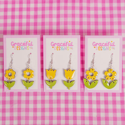 Flower-shaped earrings on cards with 'Graceful Designs' branding against a pink and white checkered background.
