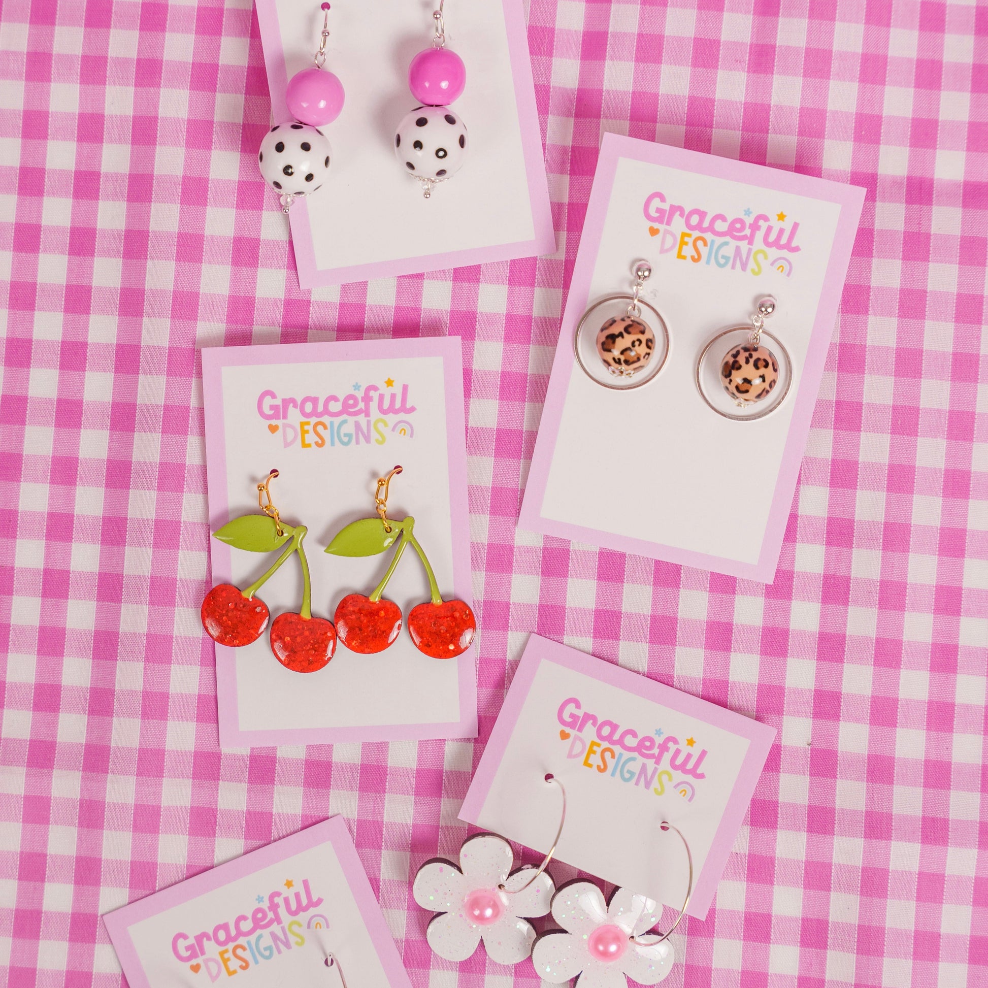 Collection of earrings on cards with 'Graceful Designs' branding on a pink checkered background.