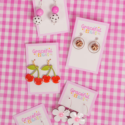 Collection of earrings on cards with 'Graceful Designs' branding on a pink checkered background.