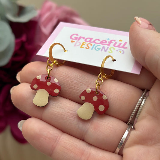 Hand holding a pair of red and gold earrings with a 'Graceful Designs' card in the background.