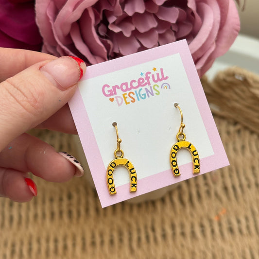 Gold horseshoe-shaped earrings on a 'Graceful Designs' card with pink flowers in the background.