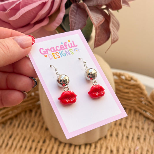 Red lip-shaped earrings on a 'Graceful Designs' card with flowers in the background