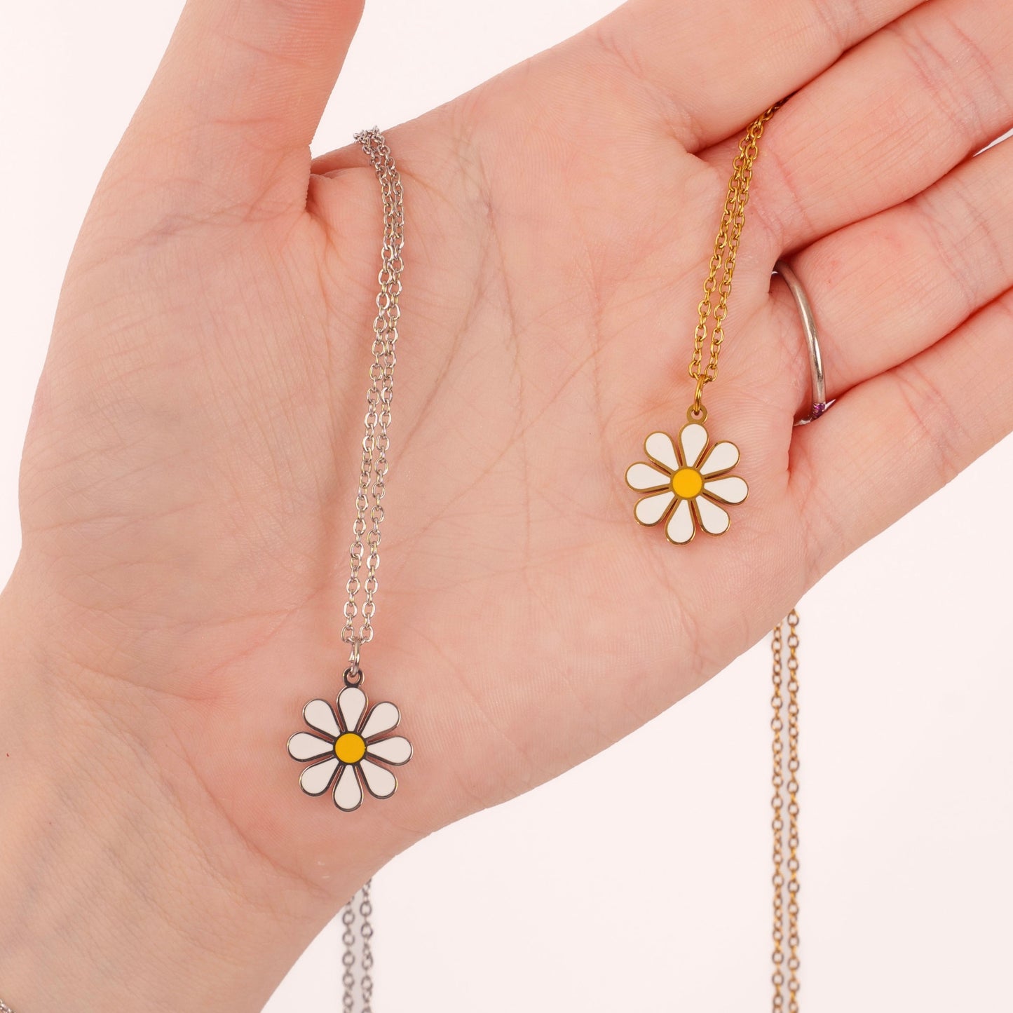 Hand wearing two necklaces with daisy pendants on a plain background