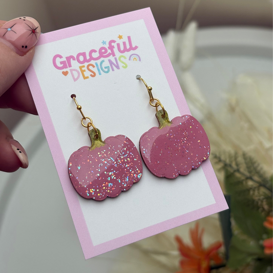 Pink glitter pumpkin earrings on a 'Graceful Designs' card held by a hand.