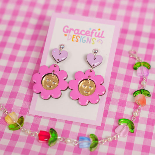 Pair of pink flower-shaped earrings on a 'Graceful Designs' card against a pink checkered background.