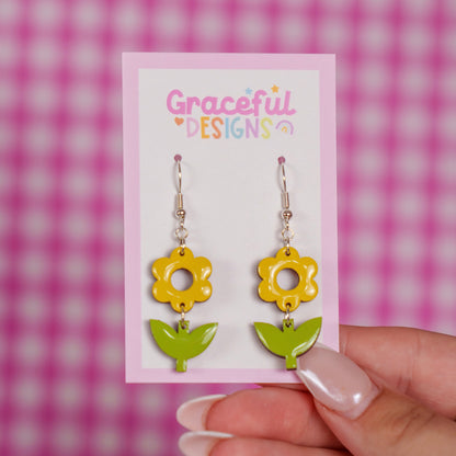 Yellow flower-shaped earrings on a 'Graceful Designs' card against a pink checkered background