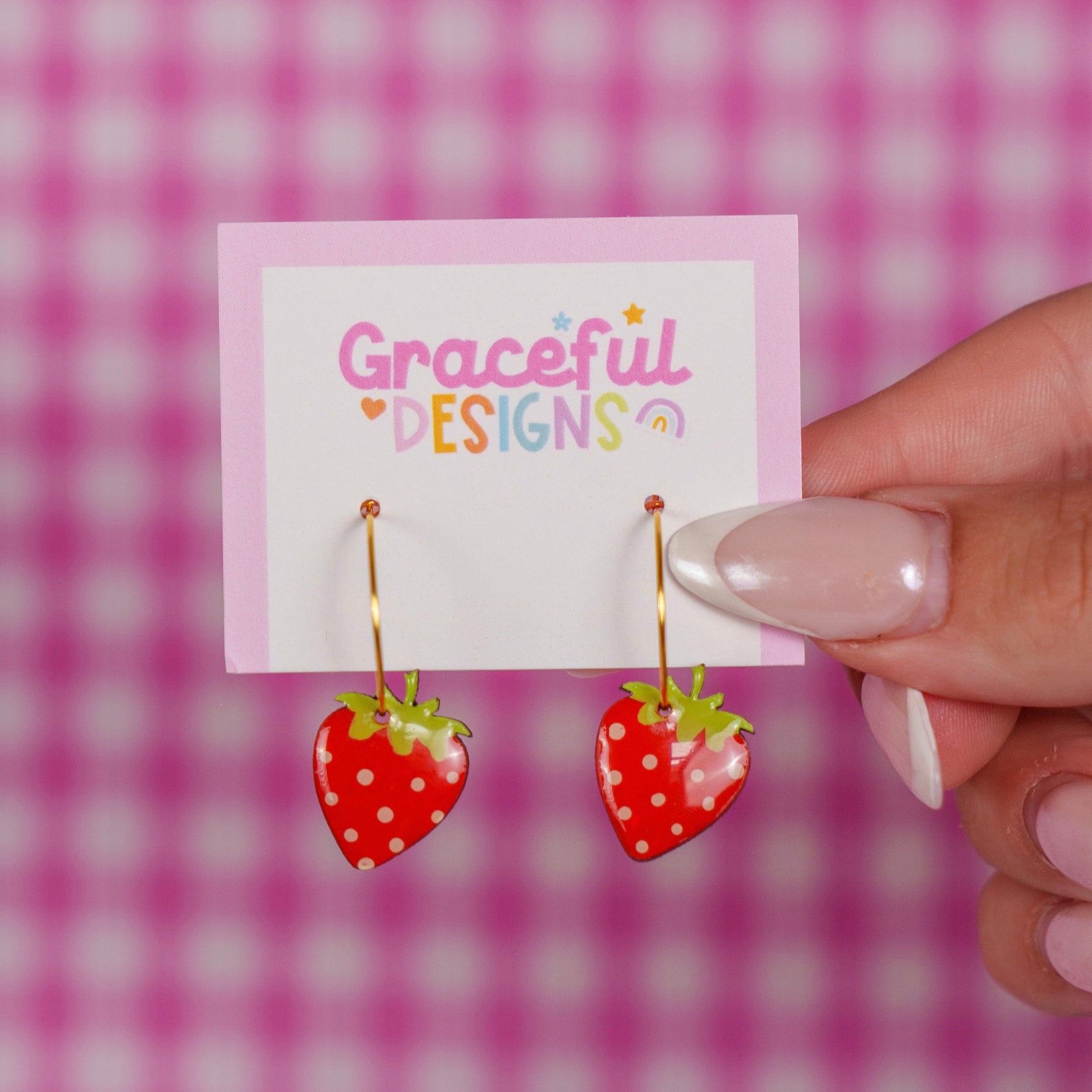 Strawberry-shaped earrings on a 'Graceful Designs' card against a pink checkered background