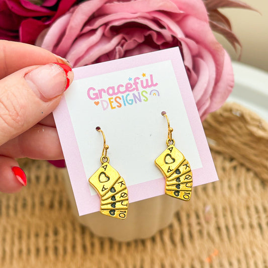 Gold earrings on a 'Graceful Designs' card with pink flowers in the background