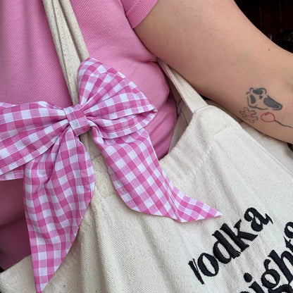 Person wearing a pink shirt with a checkered bow and holding a tote bag with text.