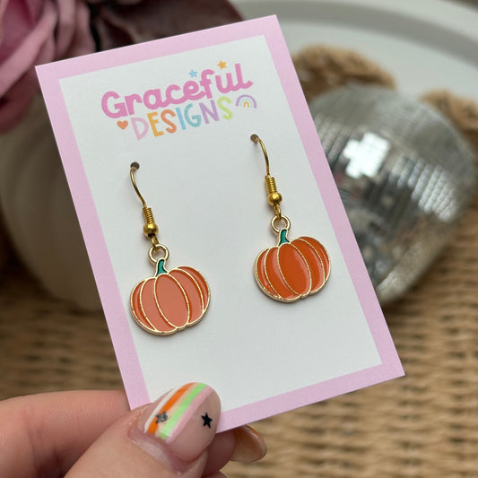 Pumpkin-shaped earrings on a 'Grateful Designs' card held by a person.