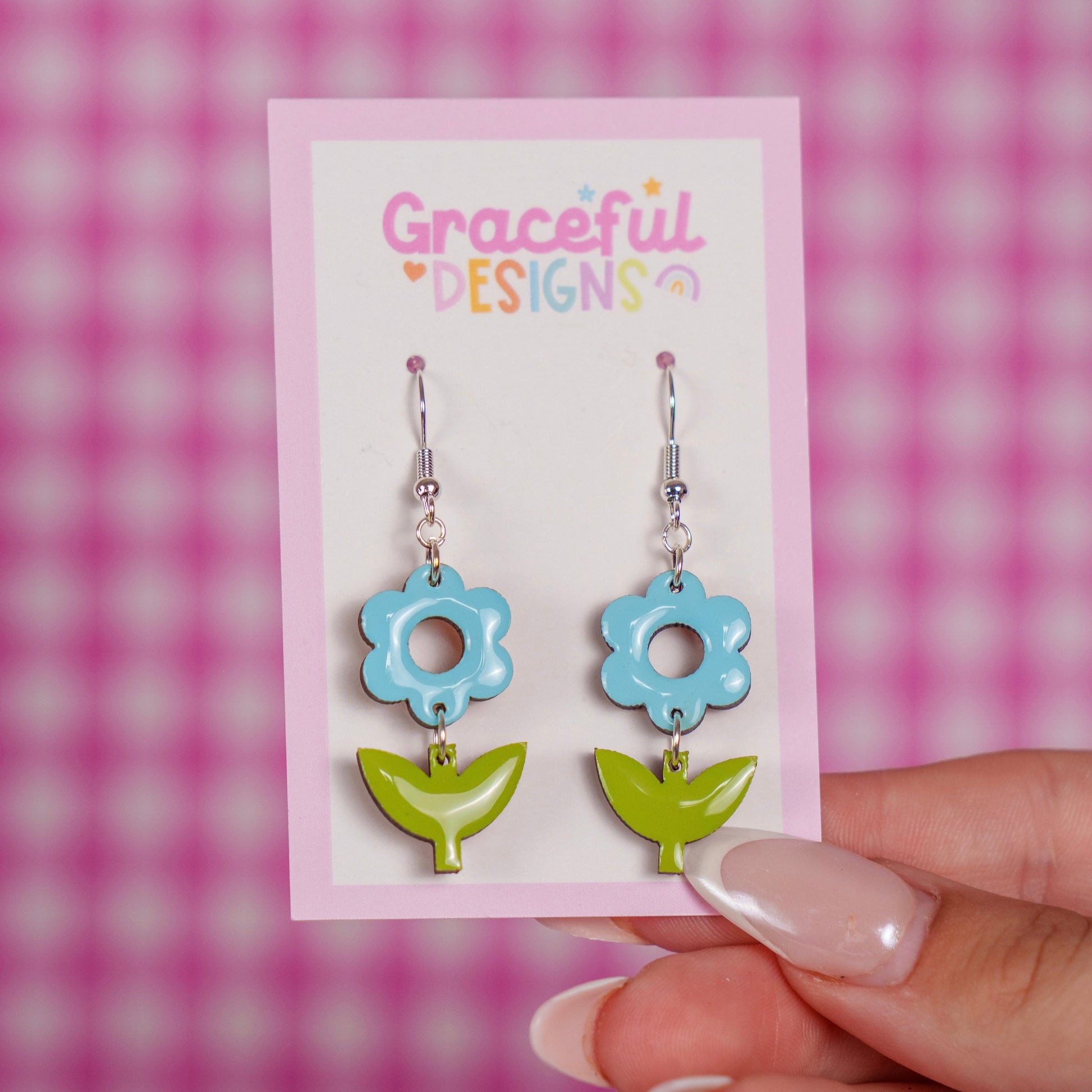 Flower-shaped earrings on a 'Graceful Designs' card against a pink checkered background