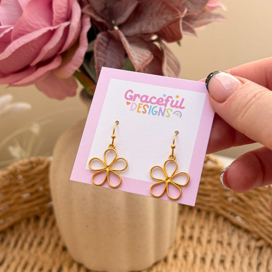 Gold flower-shaped earrings on a 'Graceful Designs' card with pink flowers in the background.