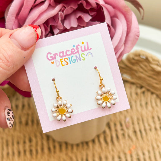 Gold flower-shaped earrings on a 'Graceful Designs' card with pink flowers in the background