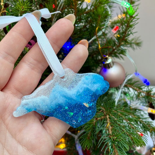 Hand holding a blue glittery ornament with a Christmas tree in the background